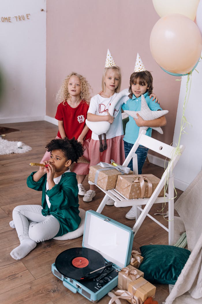 about-us A group of children enjoy a birthday party indoors with gifts, balloons, and music.