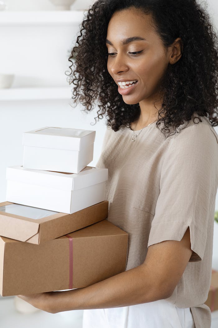 heros-img A cheerful woman holding multiple cardboard and white packages indoors, expressing happiness.
